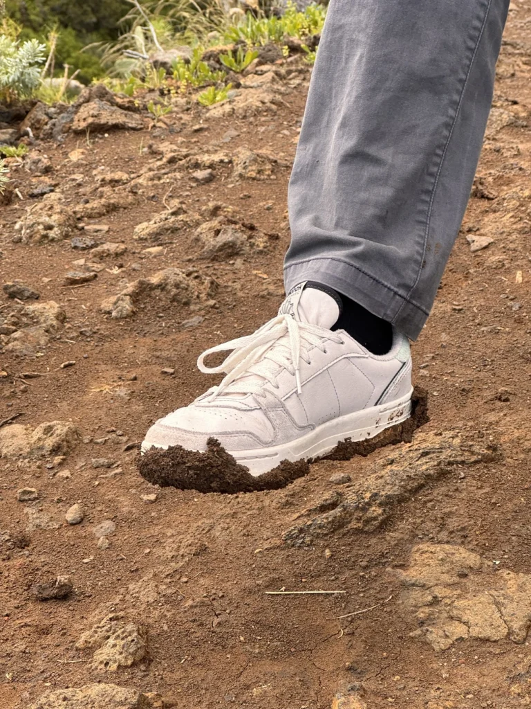 Zapatilla deportiva blanca cerrada pisando un sendero de tierra volcánica
